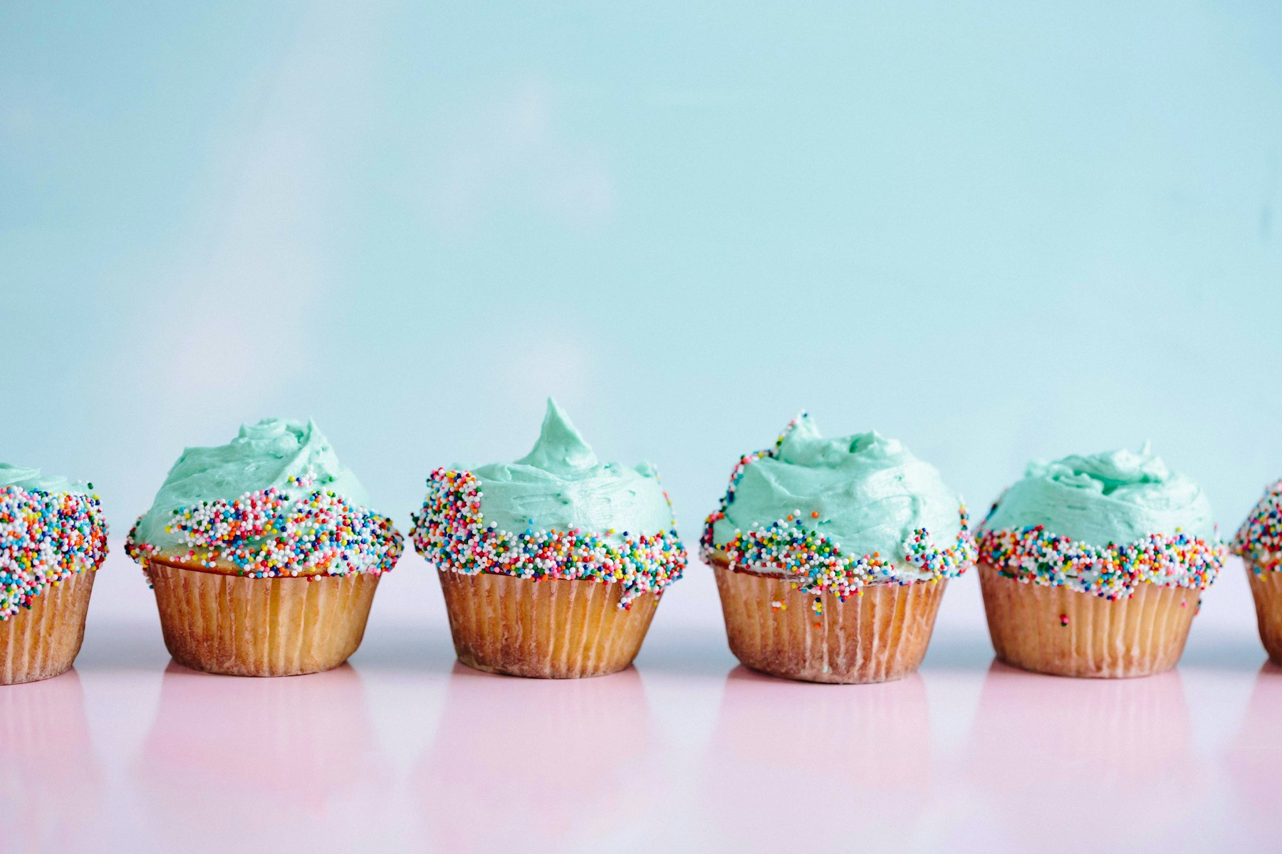 A row of sprinkle-topped cupcakes with piped blue frosting