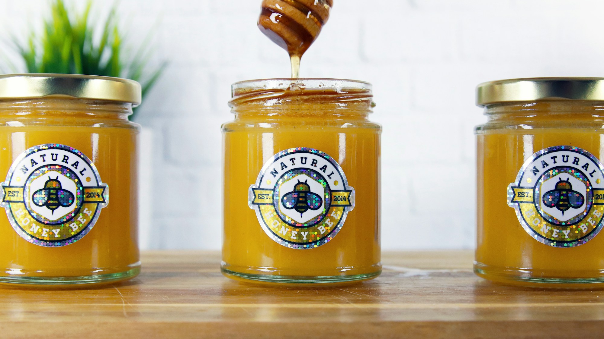 A honey dipper over a jar of honey wearing its sticker label